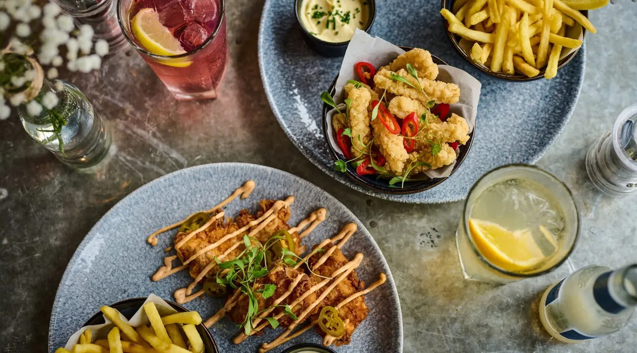 Overhead view of fried food dishes with skewered meat, calamari, chips and drinks on a table.