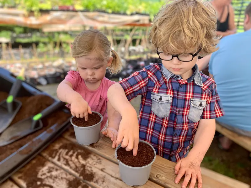 Two young children filling plant pots with compost at a garden centre or farm activity area.