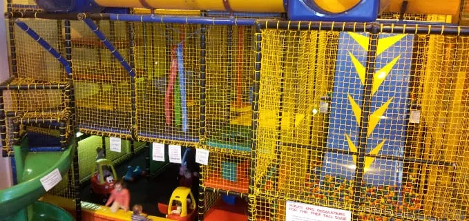 Children play in an indoor soft play area with yellow mesh netting and climbing structures.