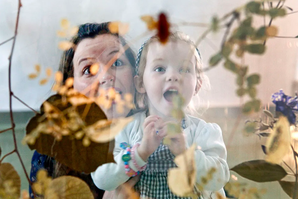 An adult and young child look delighted whilst examining plants and flowers up close in a greenhouse or botanical display.