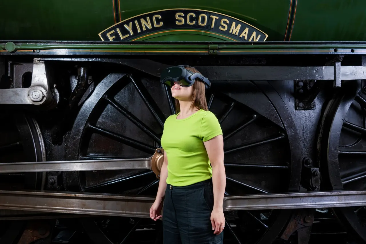 Woman wearing a VR headset stood in front of the Flying Scotsman steam locomotive.