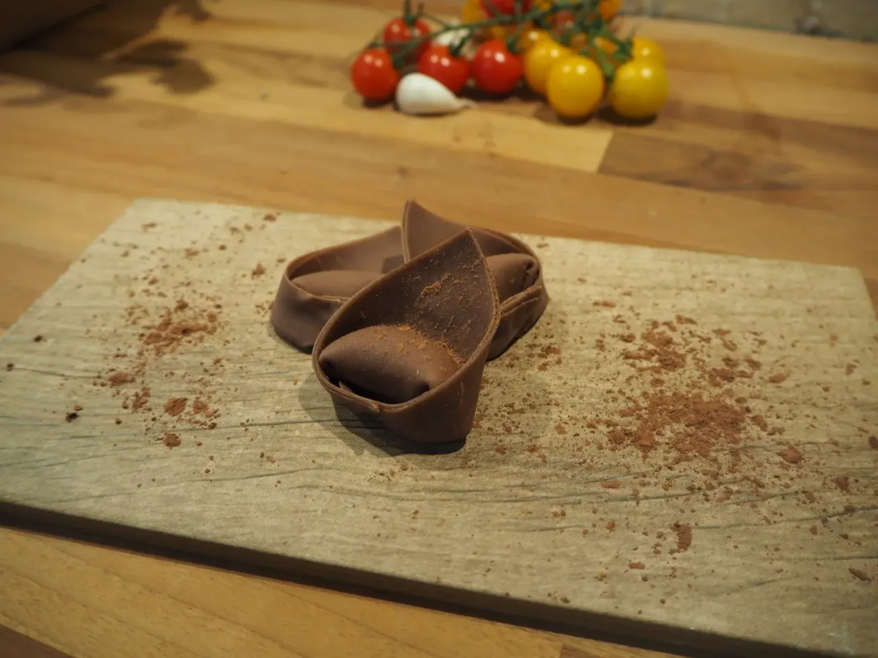Chocolate dessert with cocoa powder on a stone board, fresh tomatoes and garlic in background.