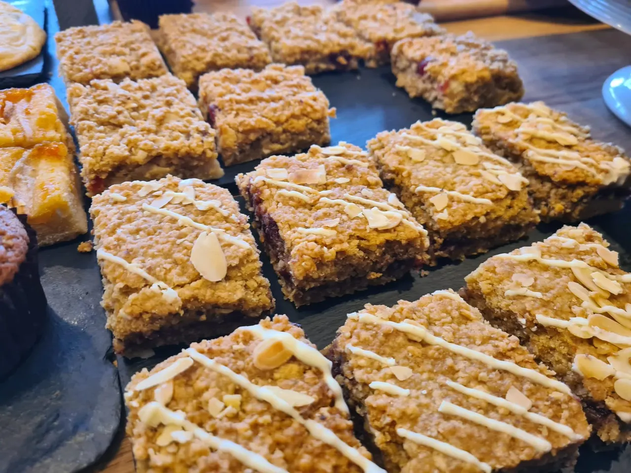 Sliced cake bars with almond topping and jam filling displayed on a dark surface.