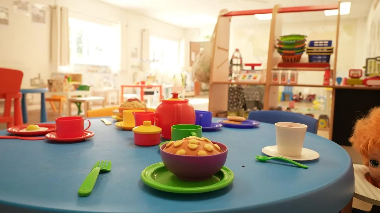 Brightly coloured play kitchen with toy food and tableware set out on a round blue table in a children's activity room.