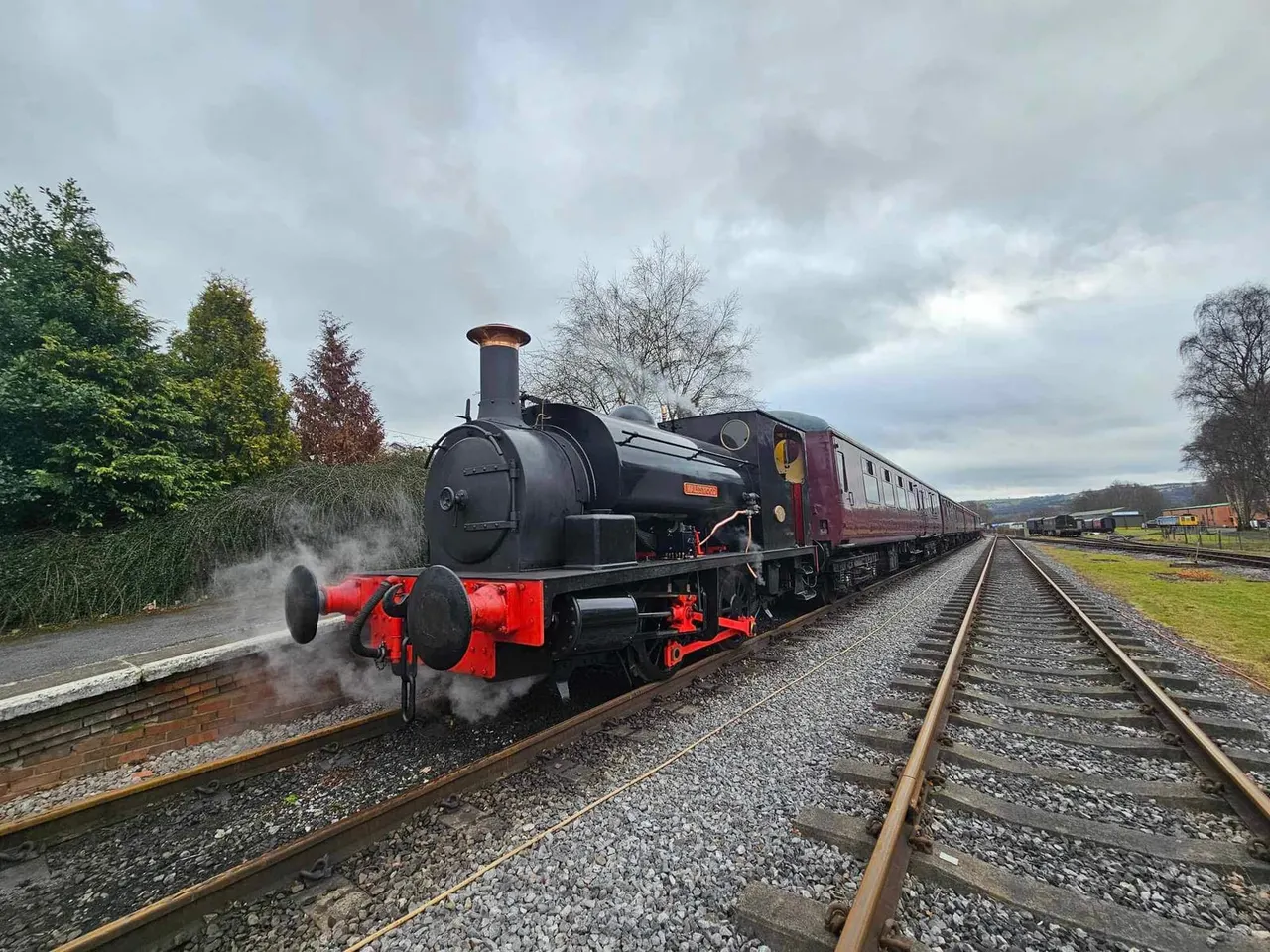 Heritage steam locomotive with red undercarriage and maroon passenger carriages on railway tracks.