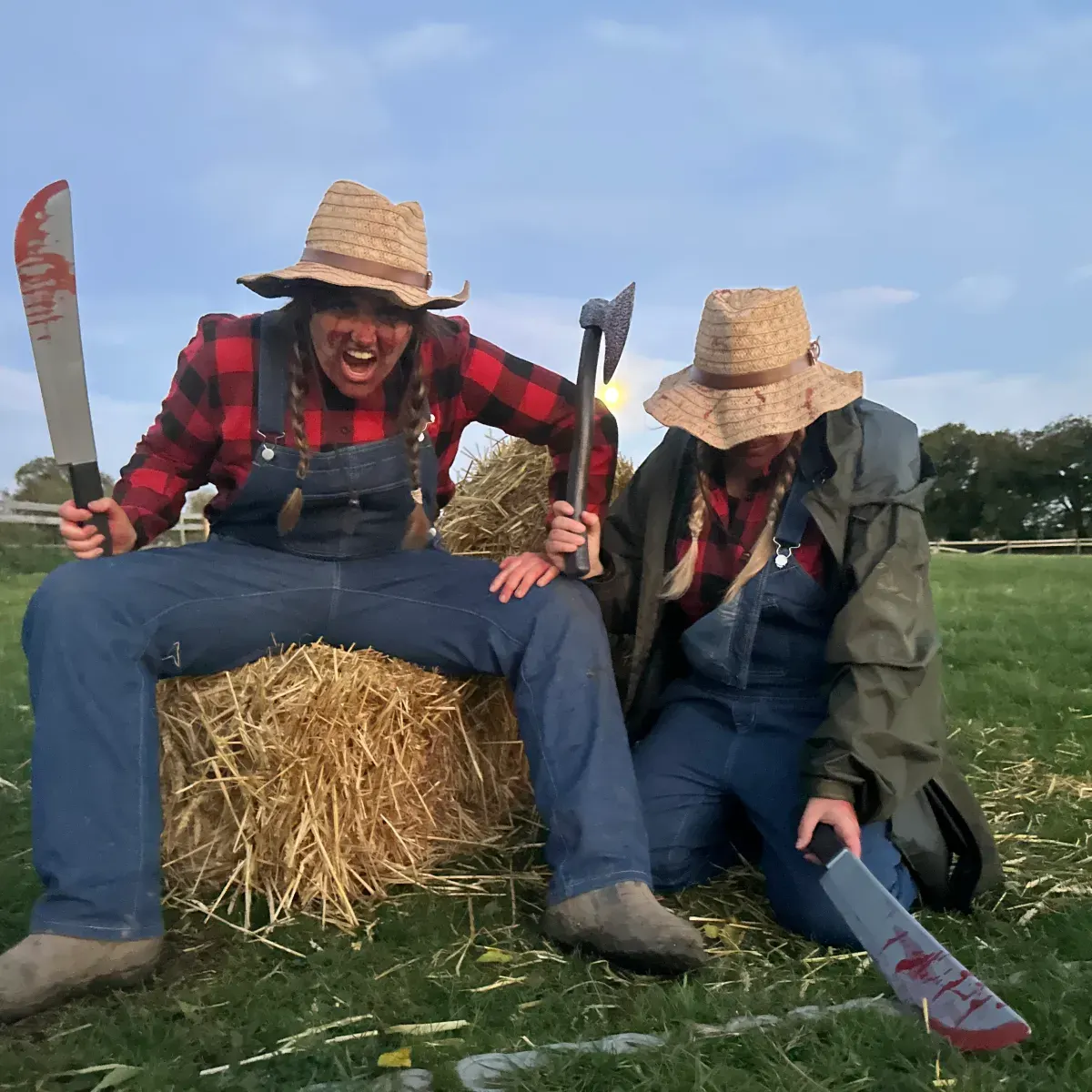 Two people in farming attire pose with a scarecrow stuffed with straw in an open field.