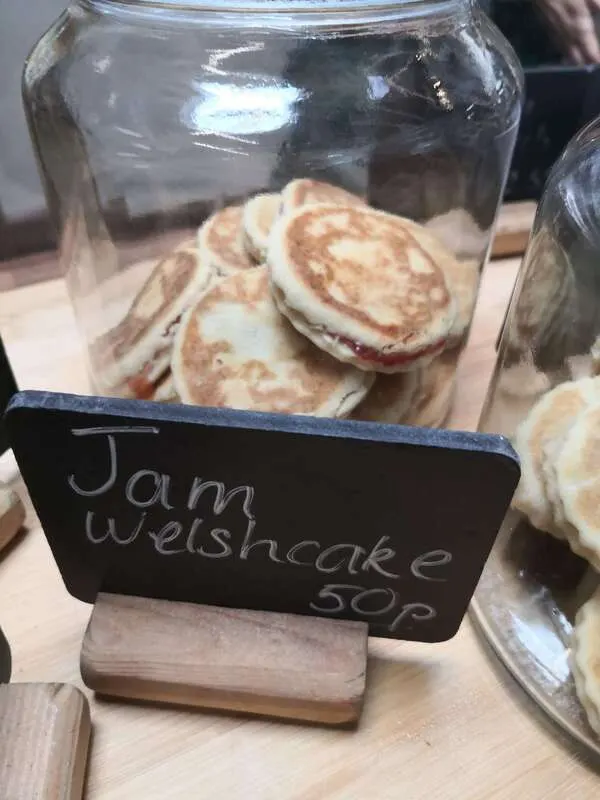 Jam welshcake scones displayed in a glass jar with a handwritten price label.