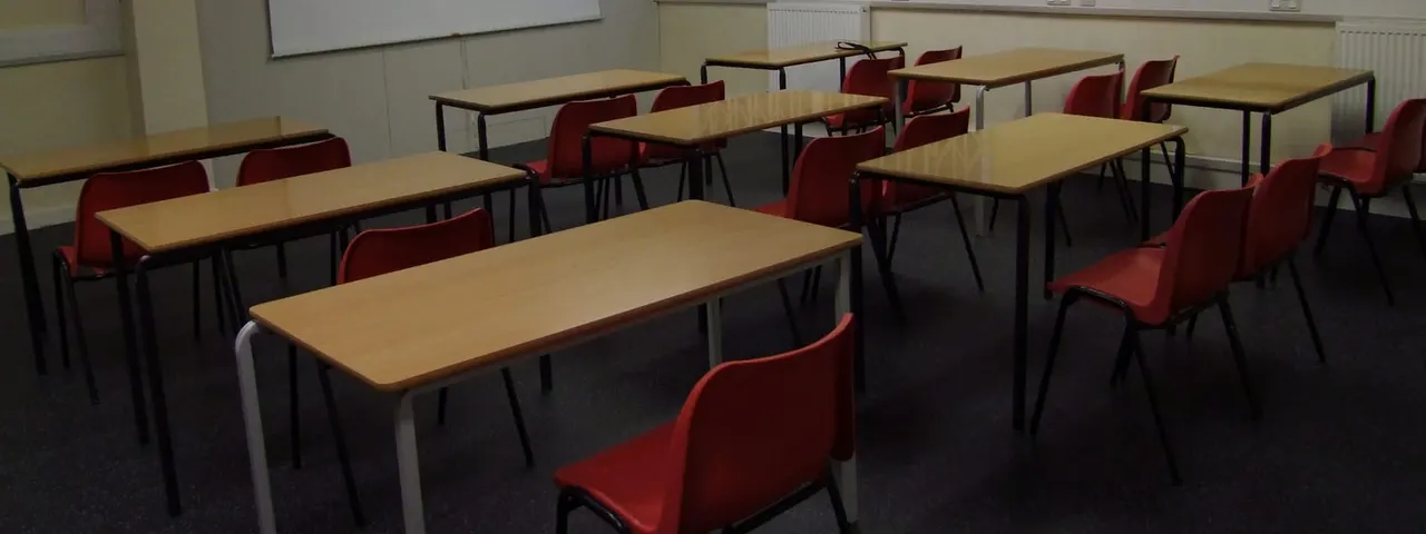 Empty dining or meeting room with wooden tables and red chairs arranged in rows.