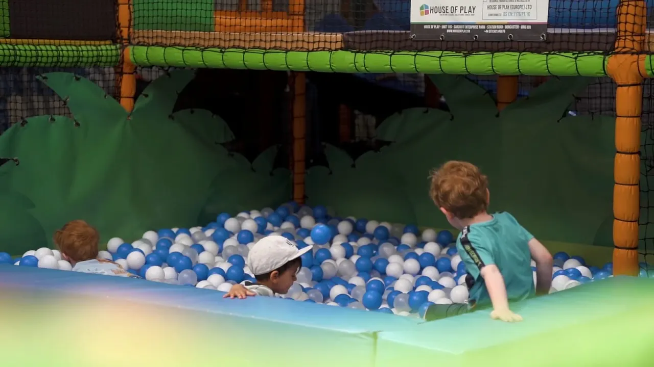 Three young children playing in a ball pit filled with blue and white balls inside an indoor play structure.