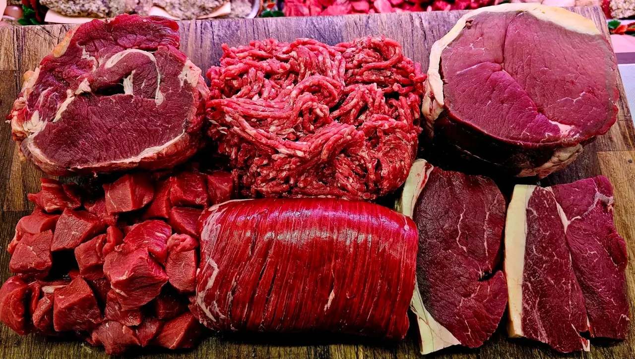 Various cuts of raw beef arranged on a wooden board, including steaks, mince and joints.