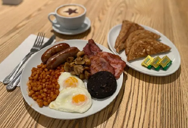 Full cooked breakfast with eggs, sausages, bacon, beans and black pudding, served with toast and coffee.
