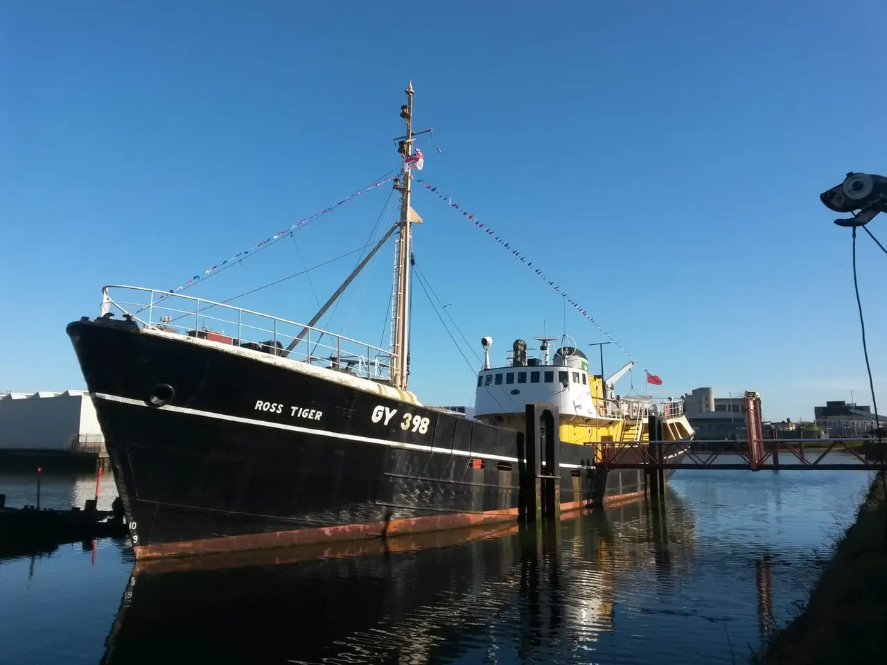 Historic fishing vessel Ross Tiger moored at a waterfront dock on a clear sunny day.