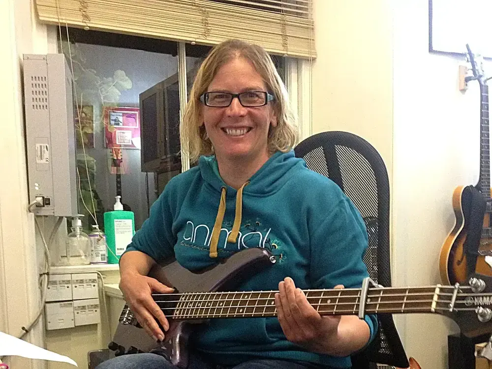 Person playing bass guitar whilst seated in a music school studio.