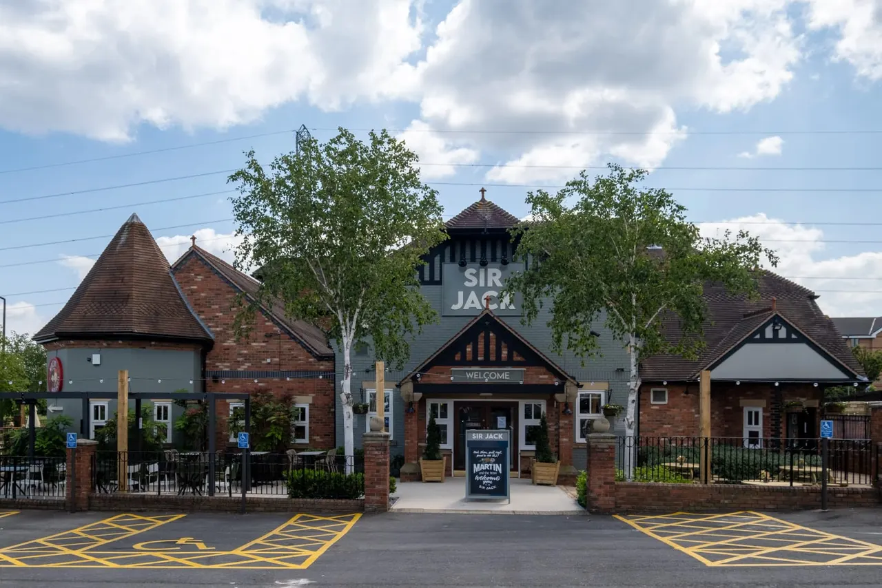 Exterior of a brick and timber-framed leisure venue with distinctive conical-roofed turrets and a tall central tower beneath a cloudy sky.