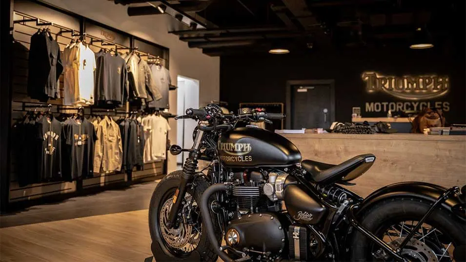 Black motorcycle on display in a retail showroom with branded clothing on wall-mounted racks and merchandise counter.