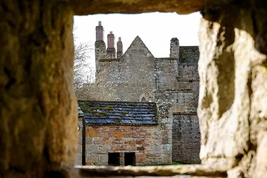 Historic stone castle viewed through a stone archway, showing chimneys and slate roof.