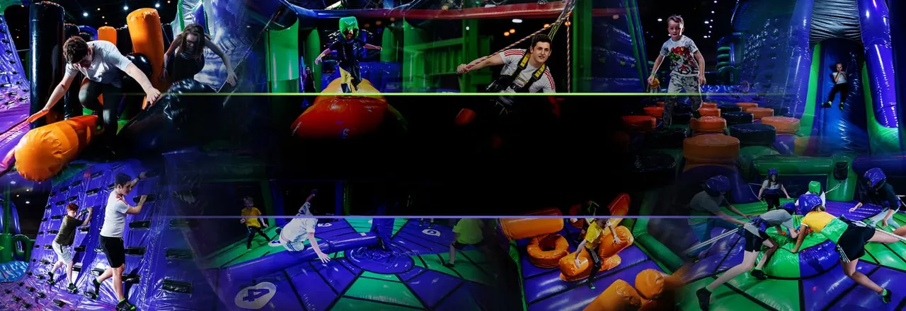 Children and adults playing on a multi-level inflatable obstacle course with neon lighting and padded obstacles.
