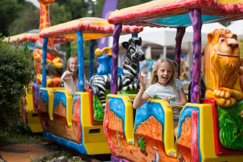 Children ride on a colourful safari-themed train attraction with animal decorations.