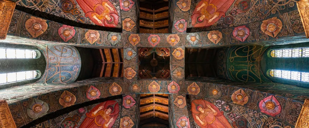 Ornate wooden ceiling beams decorated with religious iconography and colourful painted details in an interior space.
