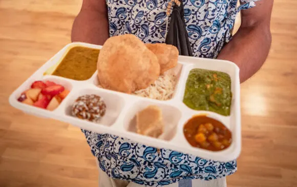 Person holding a compartmentalised tray with Indian breads, rice, vegetables and chutneys.