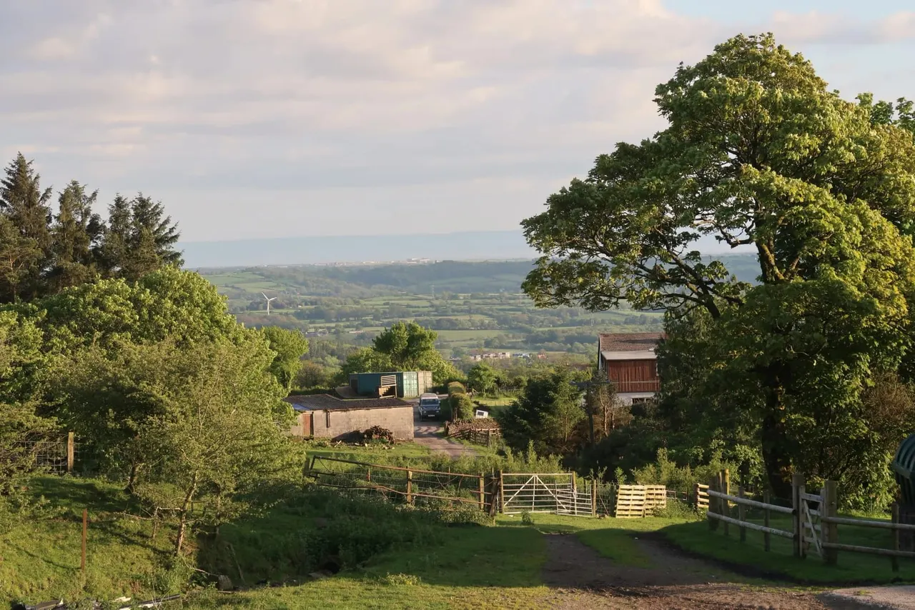Rural farm with wooden gates, brick buildings and rolling countryside landscape beyond.