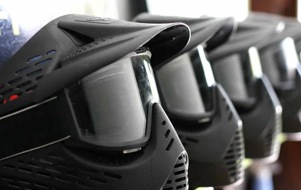 A row of black paintball masks with protective lenses lined up on a surface.