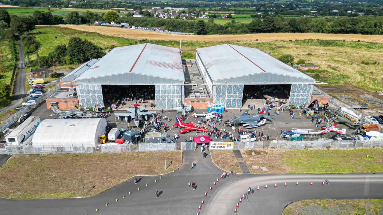 Aerial view of a hangar complex with visitors and historic aircraft on display in a rural setting.