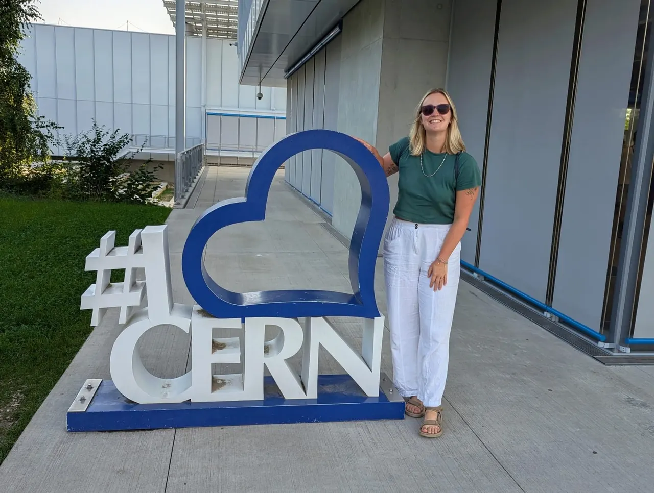 Woman posing next to a blue and white heart-shaped logo sign on a paved outdoor area.