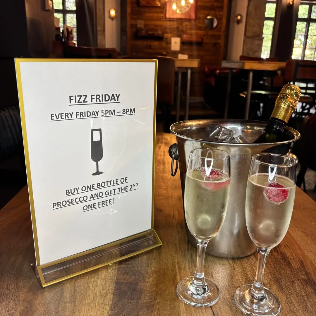 Fizz Friday promotion display with two glasses of prosecco with fruit garnishes and a bottle chilling in an ice bucket on a wooden table.
