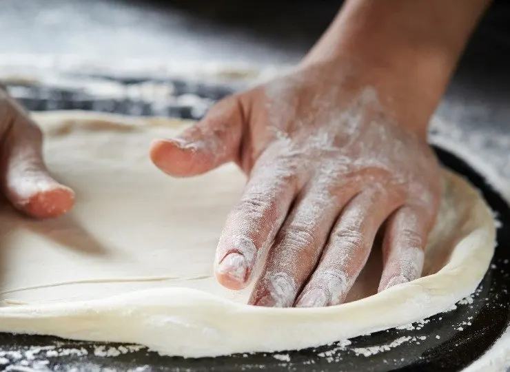 Close-up of hands kneading and stretching pizza dough on a floured surface.