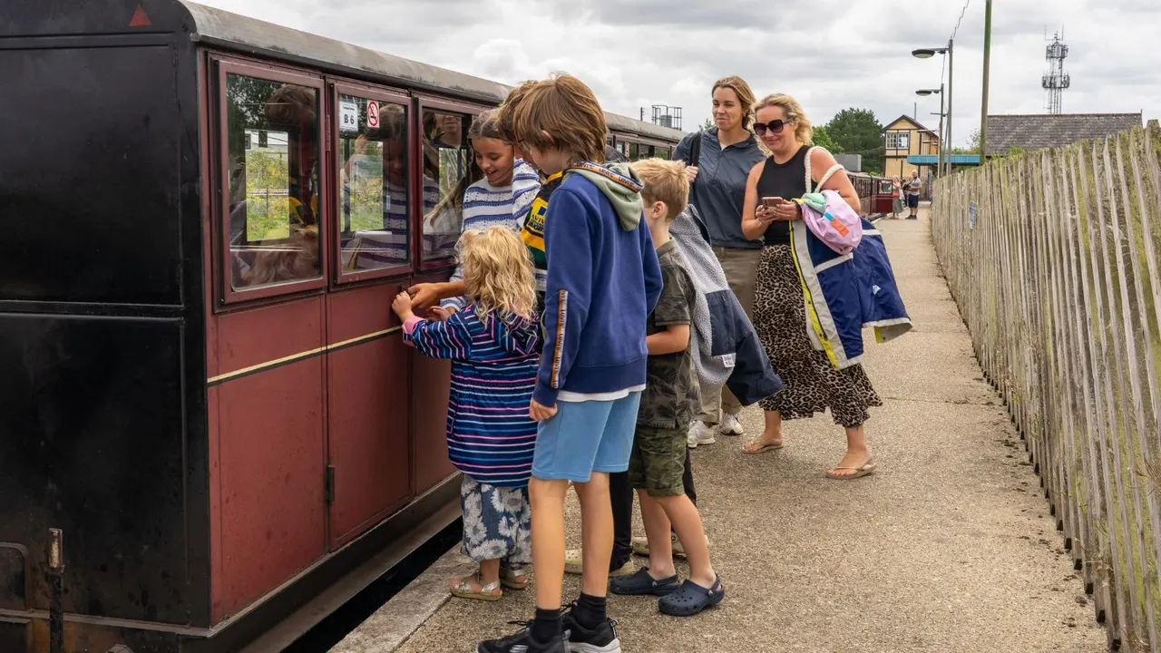 Family group queuing to board a heritage railway carriage at a station platform.