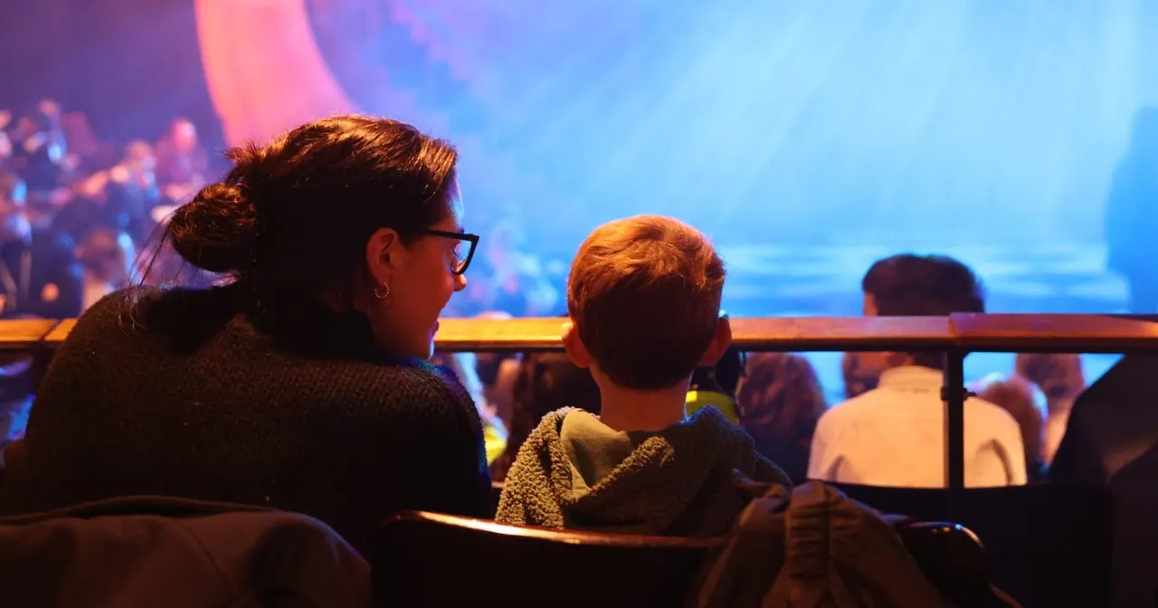 Adult and young child watching a colourful animated film on a large screen in a cinema theatre.