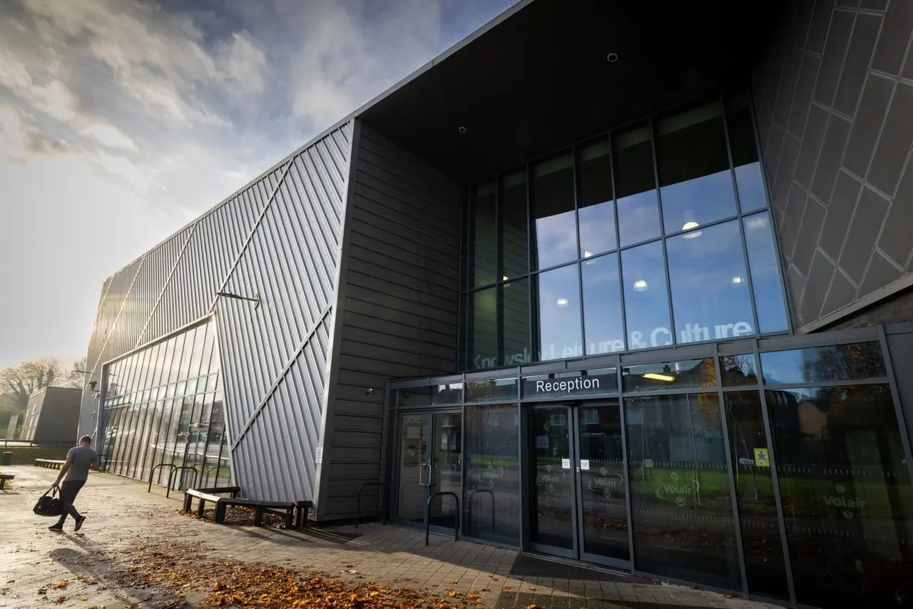 Person entering modern black and glass leisure facility with curved metal roof and reception entrance.