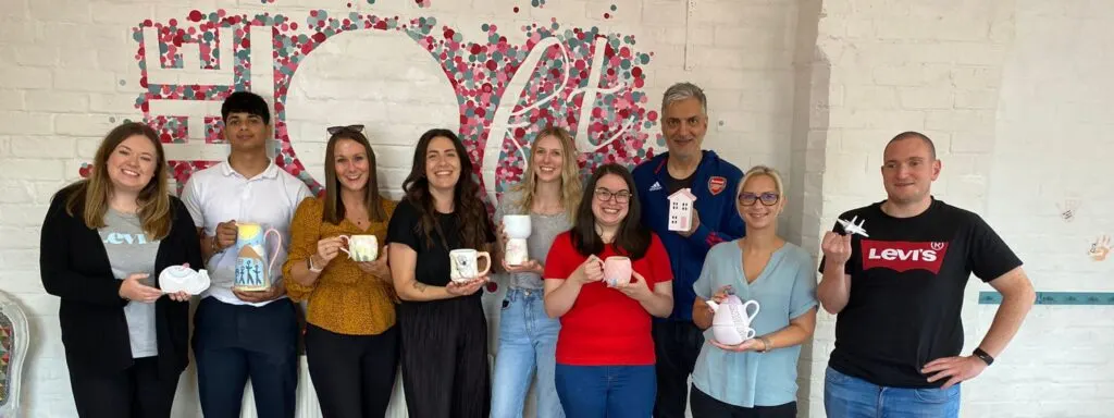A group of nine people of varying ages holding painted pottery items and smiling at a paint-your-own-pottery studio.