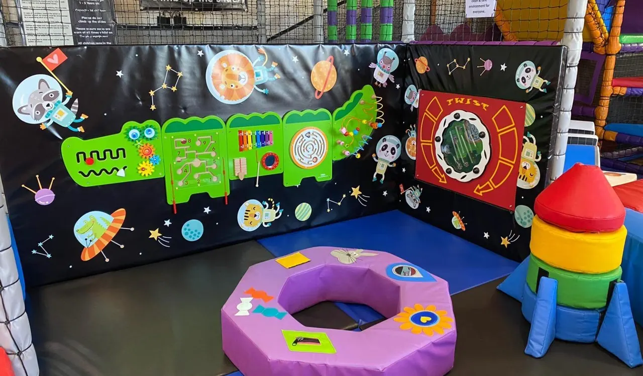 Space-themed play area with interactive activity panels, colourful foam play equipment and soft play mats for young children.