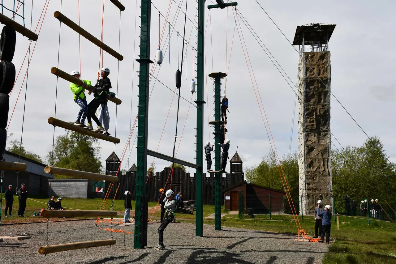 Multiple participants engaged in an outdoor adventure course with rope obstacles and a tall climbing tower.
