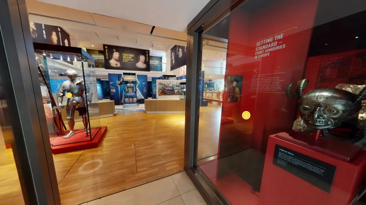Museum gallery displaying suits of armour and metal helmet artefacts in glass cases with blue and red exhibition panels.