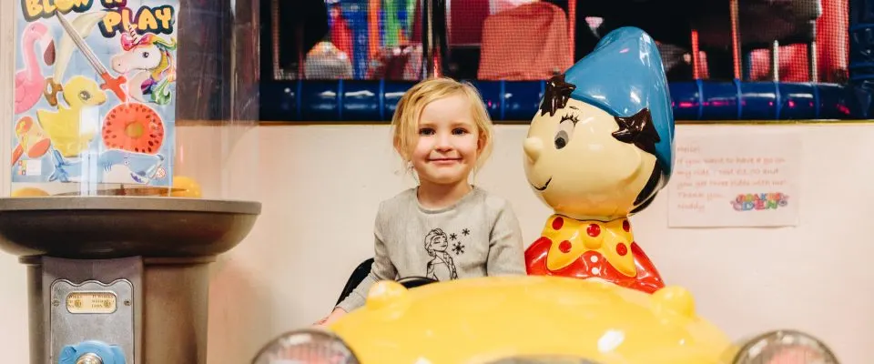Young child posing with a costumed character next to a large yellow vehicle prop.