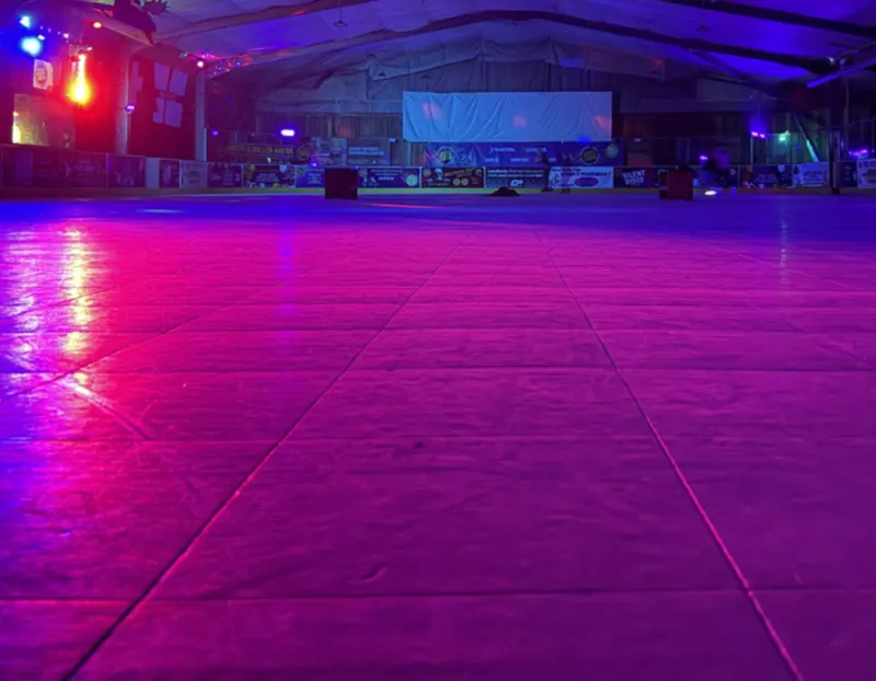 An empty roller skating rink with purple and pink neon lighting illuminating the polished wooden floor.