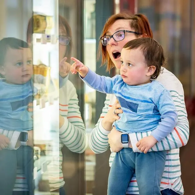Woman and young child looking at a glass display case in a museum, child pointing at the exhibit.