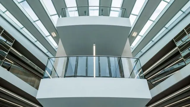 Modern white building interior viewed from below showing curved balconies and skylights with geometric architectural design.