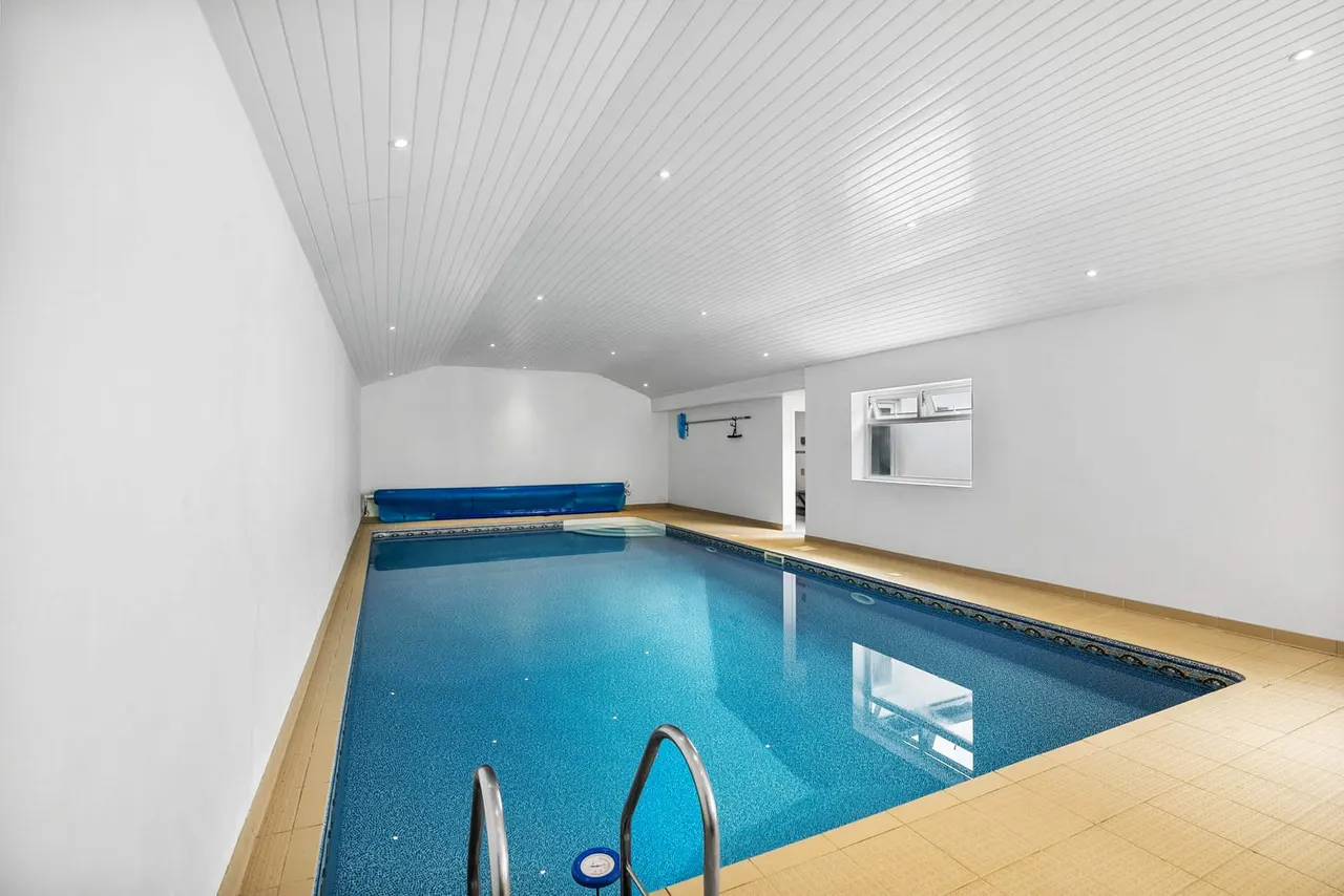 Indoor swimming pool with blue water, wooden surround, white walls and ceiling with recessed lighting.