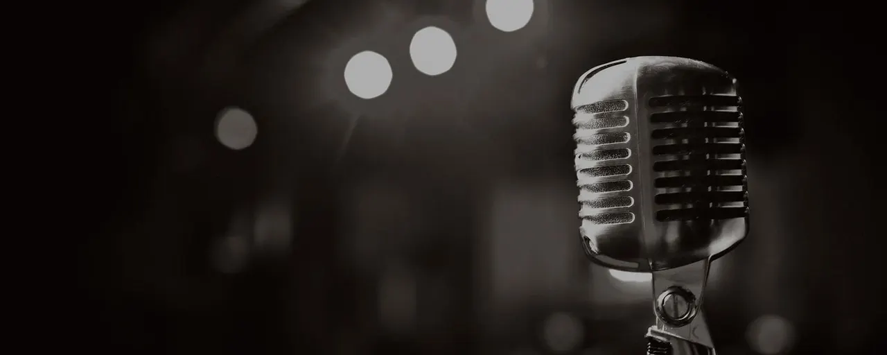 Vintage microphone in black and white against blurred stage lights in darkness.