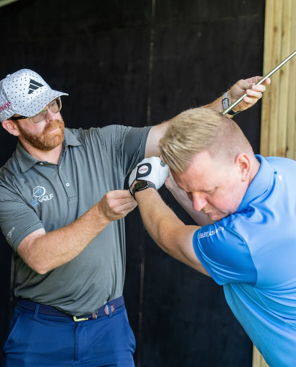 Golf instructor adjusting the grip of a male golfer during a lesson indoors.