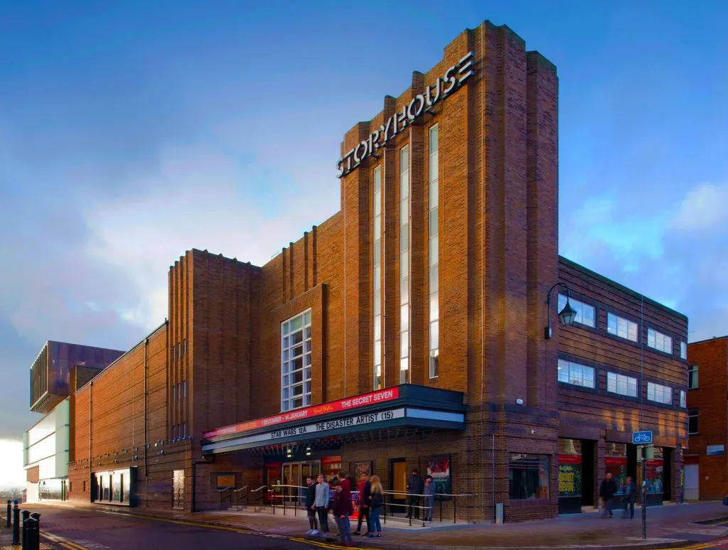 Art deco brick building with vertical white stone bands and "Storyhouse" signage, with people standing outside the entrance at dusk.