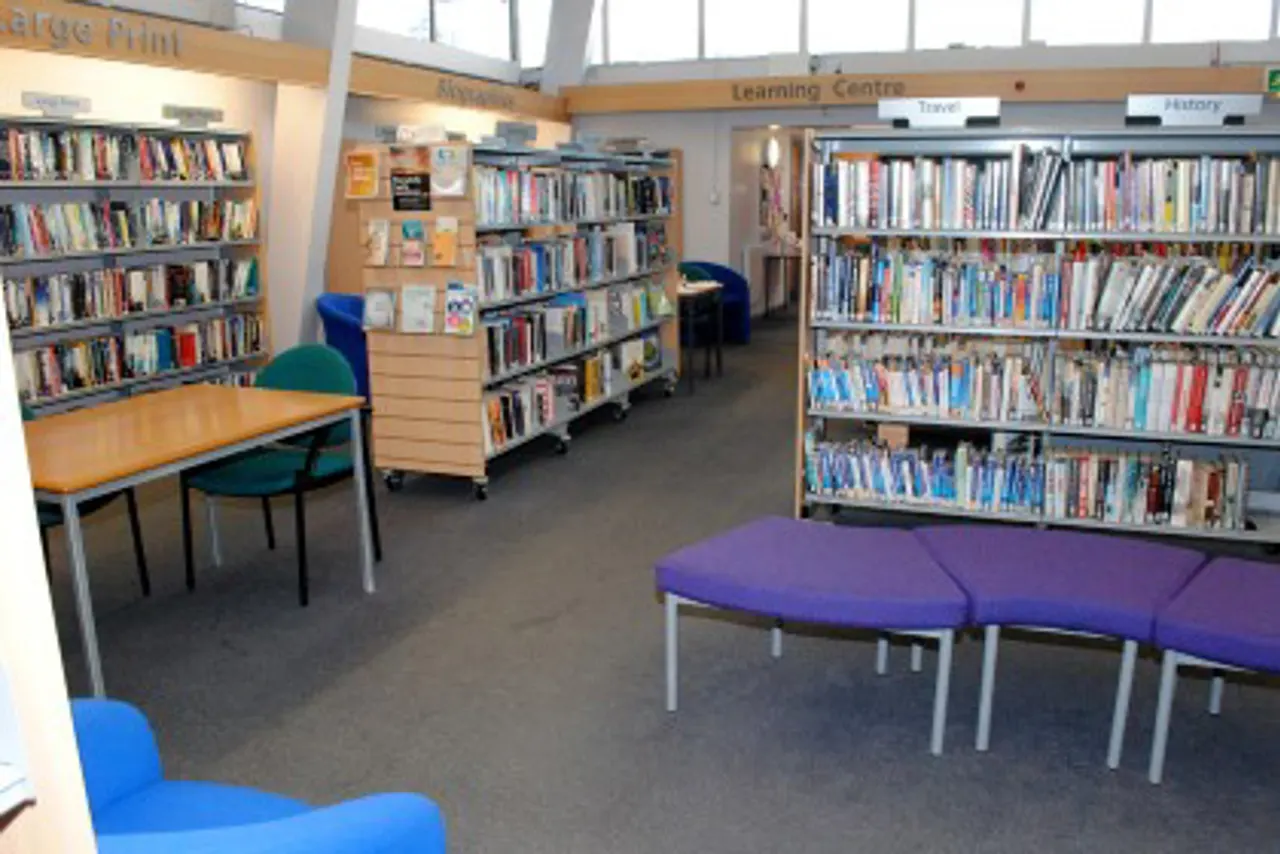 Interior of a learning centre with bookshelves, reading tables with coloured chairs, and purple seating pods.