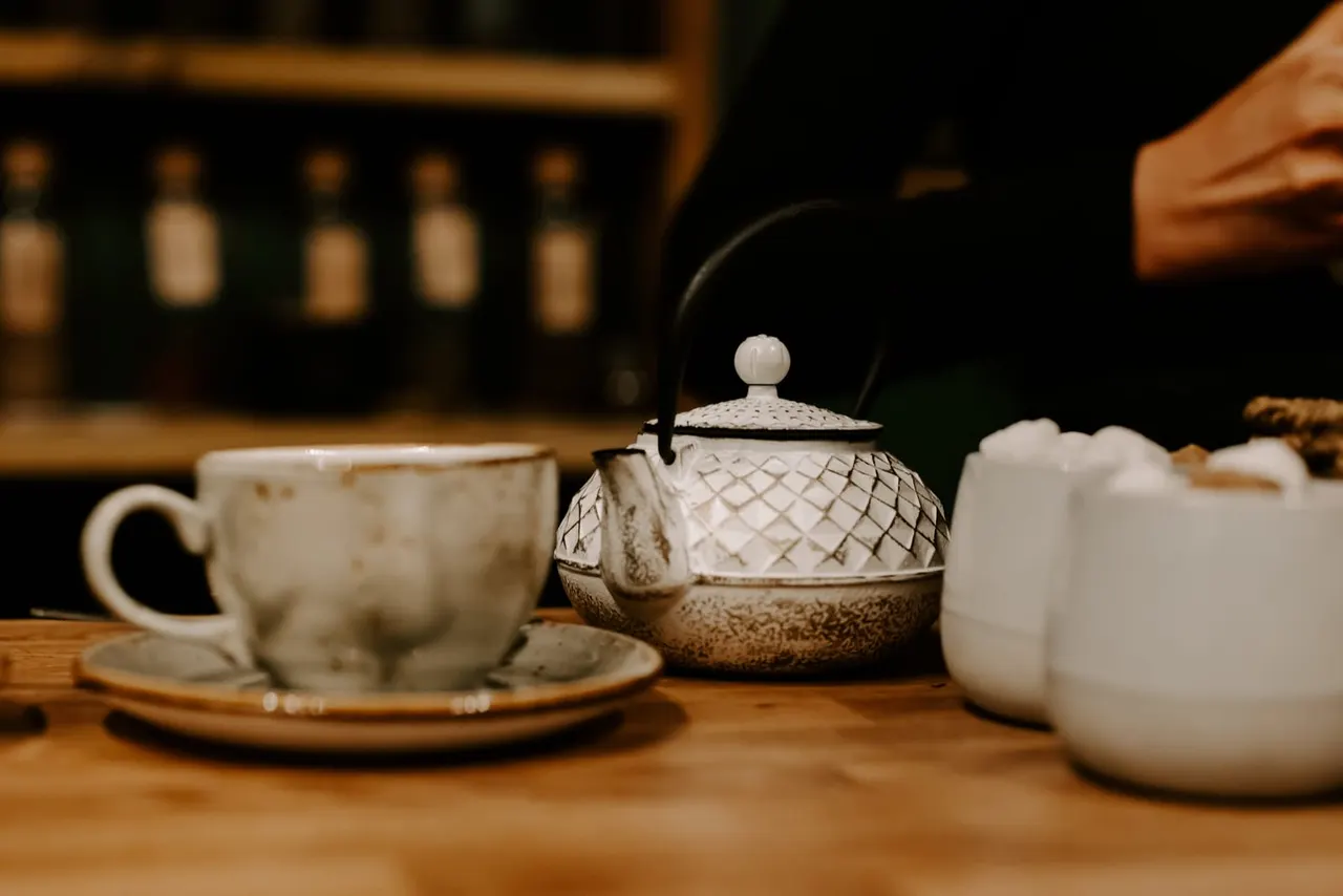 Ceramic teapot and cup with saucer arranged on a wooden table in a tea house setting.