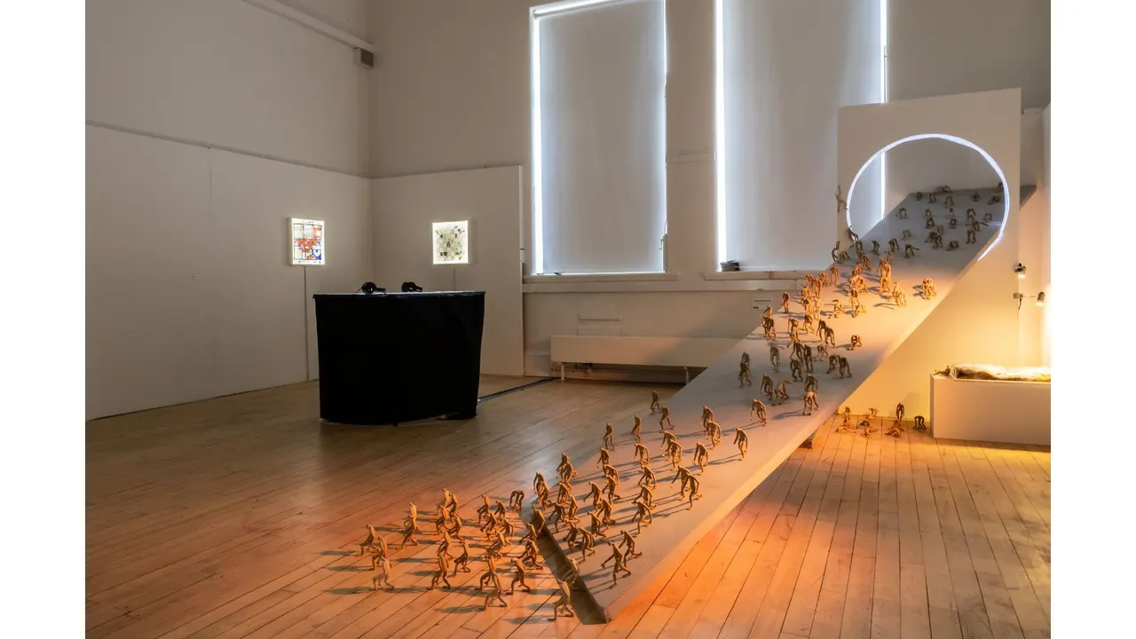 Modern art gallery interior with golden figurative sculptures arranged on wooden flooring and elevated platforms under bright natural light.