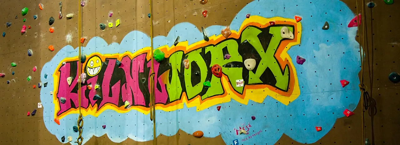 Indoor rock climbing wall with colourful painted design and numerous climbing holds in various colours.