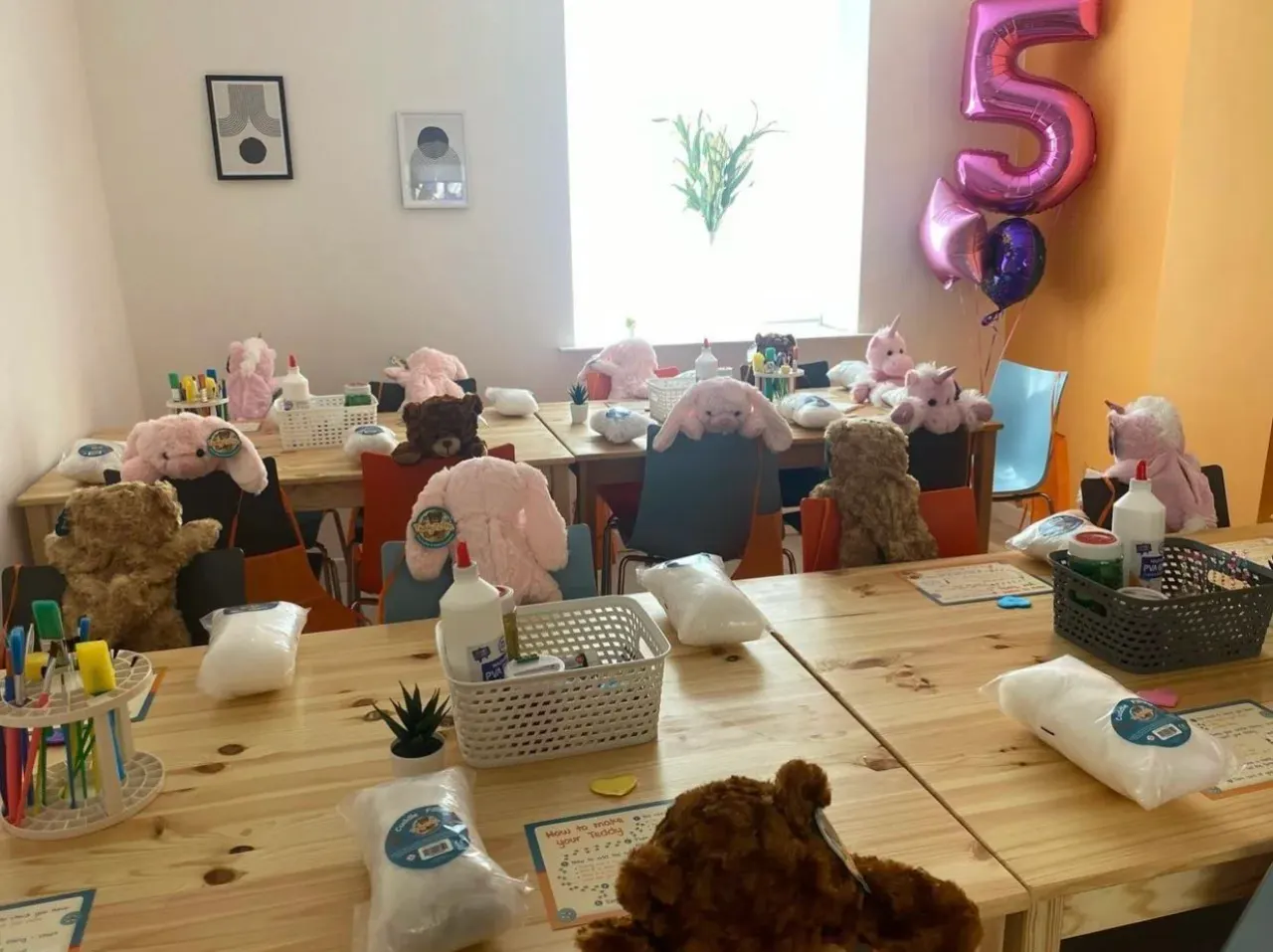 Craft activity room with stuffed animals seated at tables, craft supplies, and a number 5 balloon decoration.